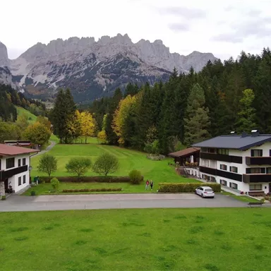 A picturesque landscape with two beautiful buildings and lush green grass. In the background, majestic mountains rise up.