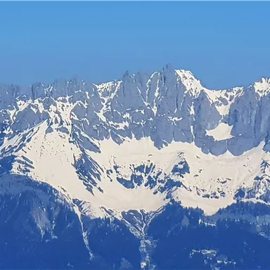 Ein majestätisches Bergpanorama mit schneebedeckten Gipfeln. Der klare blaue Himmel ergänzt die beeindruckende Landschaft.