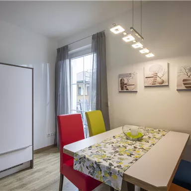 A modern kitchen with a dining table and colorful chairs. Three pictures hang on the wall, and the light is bright and inviting.