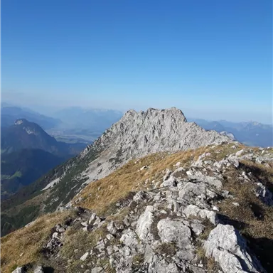 Ein beeindruckender Berg mit steilen Felsen und klarem blauen Himmel. Die Landschaft ist grün und bietet eine weite Aussicht.