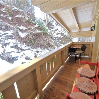 A cozy balcony with a red seating area and a small table. In the background, snow-covered mountains are visible.