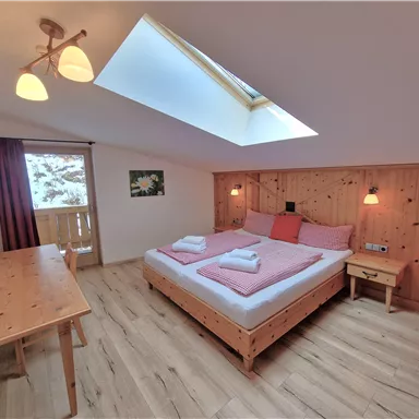 A cozy bedroom with a double bed and wooden decor. There is a large window and a desk in the room.