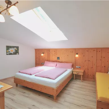 A cozy room with a double bed and a seating area. The walls are made of wood and a skylight provides plenty of daylight.