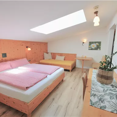 A cozy bedroom with a double bed and a sofa bed. The room has bright walls, wooden paneling, and plenty of natural light.