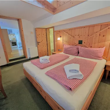 A cozy bedroom with a large bed and wood paneling. The room is bright and inviting, with a table and chairs.