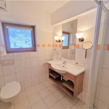 A modern bathroom with a shower, sink, and mirror. The walls are brightly tiled, and there is a window that lets in daylight.