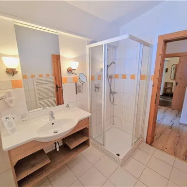 A modern bathroom with a shower cubicle and a sink. The walls are tiled in light colors and there are wood details in the room.