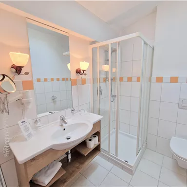 A modern bathroom with a shower, sink, and toilet. It is bright and friendly with tiles in white and orange.