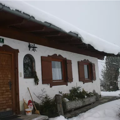 A traditional house in the snow, surrounded by a winter landscape. The layer of snow gently rests on the roof and the plants.  The house is located just above the mountain station of the  Hausberglift  and directly on the slope from Astberg to Ellmau. The house can be reached also in winter with snow tires and snow chains