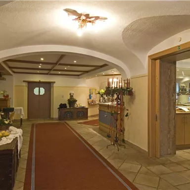 An inviting entrance area with a carpet and warm light. On the left side are decorative furniture and plants.