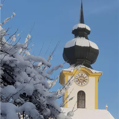Eine Kirche mit einer markanten Spitze, bedeckt von Schnee. Der Himmel ist blau und klar.