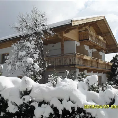 Ein charmantes Holzhaus im Winter, umgeben von frischem Schnee. Die Balkone sind im traditionellen Stil gestaltet und das Licht scheint durch die Wolken.