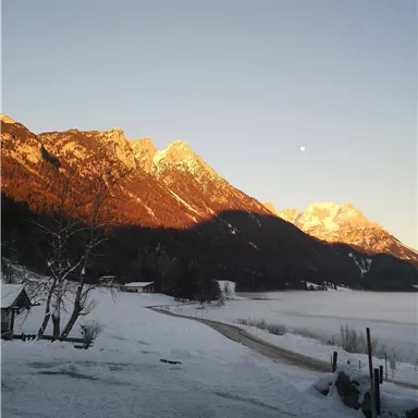 Eine winterliche Landschaft mit schneebedeckten Bergen und einem klaren Himmel. Sanftes Sonnenlicht beleuchtet die Berge im Hintergrund.