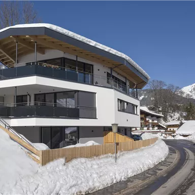Ein modernes Haus in den Bergen, umgeben von Schnee. Im Hintergrund sind schneebedeckte Berge zu sehen.