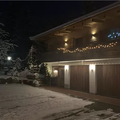 A cozy house in the snow, illuminated by warm lights. The surroundings are wintry and inviting.