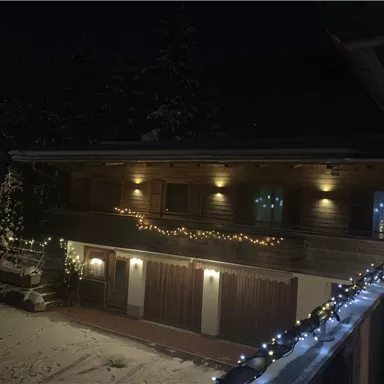 A cozy chalet in the snow, illuminated with festive lights. The night sky creates a cozy atmosphere.