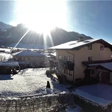 Eine verschneite Landschaft mit einem großen Sonnenstrahl im Hintergrund. Im Vordergrund sind einige Häuser und Berge sichtbar.