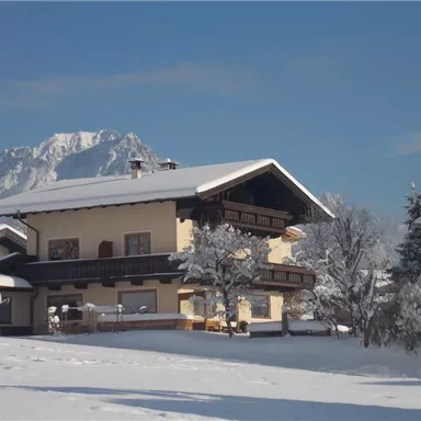 Ein schönes Haus in einer schneebedeckten Landschaft. Im Hintergrund sind schneebedeckte Berge sichtbar.