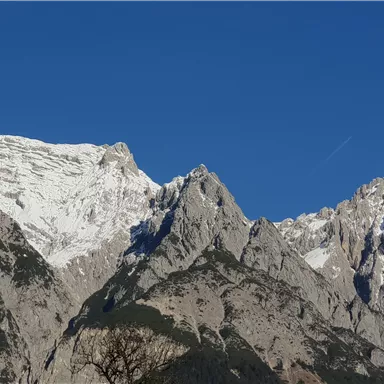 Eine majestätische Berglandschaft mit schneebedeckten Gipfeln und klarem, blauem Himmel. Die Felsen zeigen beeindruckende Formationen und sind von einer schönen Natur umgeben.