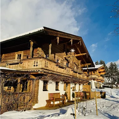 Ein traditionelles Holzhaus im Schnee mit einem großen Balkon. Der Himmel ist klar und die Umgebung strahlt winterliche Ruhe aus.