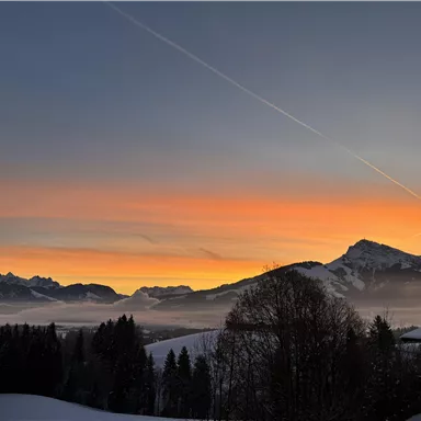 Ein wunderschöner Sonnenaufgang über schneebedeckten Bergen. Die Farbpalette reicht von Orange bis Blau am Himmel.