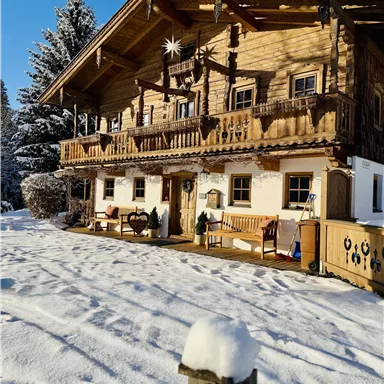 Ein traditionelles Holzhaus im Schnee mit einem gemütlichen Balkon. Die Umgebung ist winterlich und friedlich.