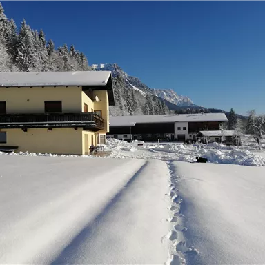 Ein gemütliches Haus in einer verschneiten Landschaft. Der Himmel ist klar und die Umgebung ist von frischem Schnee bedeckt.