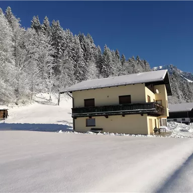 Ein Haus im Schnee mit umgebenen verschneiten Bäumen. Der Himmel ist klar und blau.