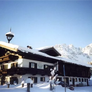 A charming mountain house in winter, covered with snow. Impressive mountains can be seen in the background.