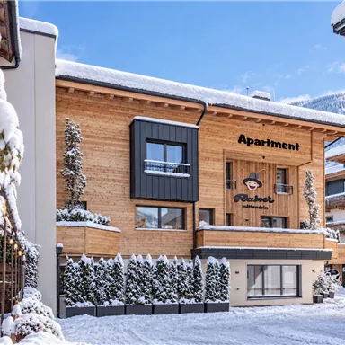 A cozy apartment building in winter, surrounded by fresh, fallen snow. The wooden facade gives it an inviting charm.