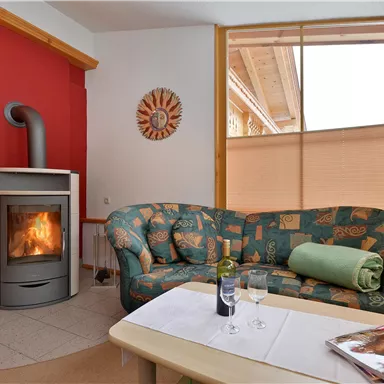 A cozy living space with a green sofa and a modern fireplace. The room has bright windows and a warm atmosphere.