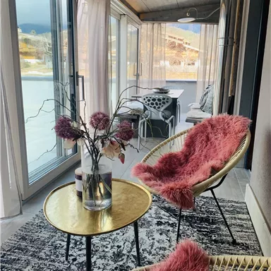 Eine stilvolle Veranda mit modernen Möbeln. Ein runder Tisch mit einer Vase und gemütlichen Stühlen bietet einen einladenden Blick nach draußen.