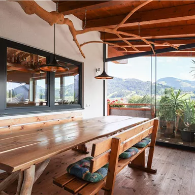 A cozy dining area with a large wooden table and benches. Through the windows, you can see the mountains and nature outside.