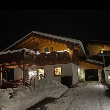 Ein gemütliches Haus im Schnee, beleuchtet von warmen Lichtern. Die Umgebung ist ruhig und winterlich.
