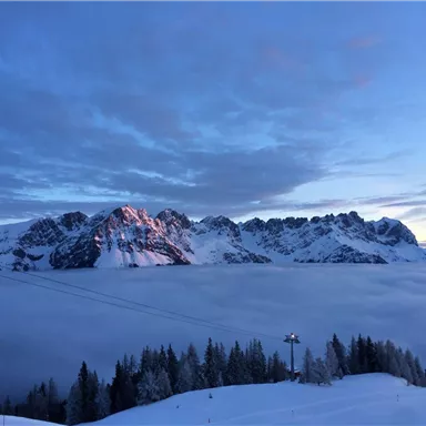 A majestic mountain landscape with snow-covered peaks. Below, a blanket of clouds spreads out, while the sky is gently blue and cloudy.