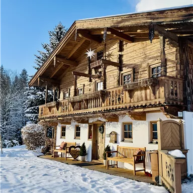 Ein gemütliches Holzhaus im Winter, umgeben von Schnee und Tannenbäumen. Die Balkone sind mit Weihnachtsdekoration geschmückt.