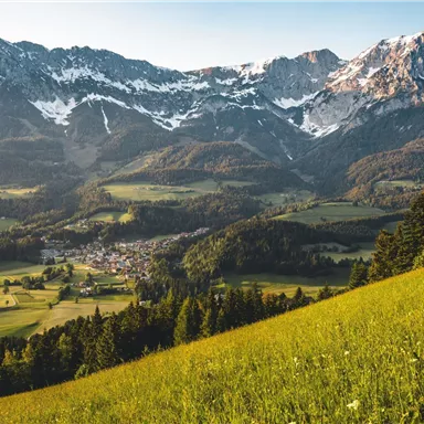 An impressive mountain landscape with snow-capped peaks and green meadows. In the valley lies a small village, surrounded by nature.