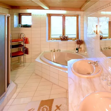 Ein modernes Badezimmer mit einer freistehenden Badewanne und einer Dusche. Helle Fliesen und Fenster sorgen für eine freundliche Atmosphäre.