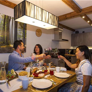 Ein gemütliches Abendessen mit Freunden in einer modernen Küche. Die Tischdekoration enthält leckeres Essen und Getränke, während alle anstoßen.