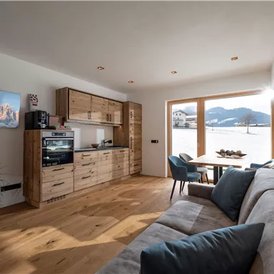 A modern living room with wooden shelves and a cozy couch. Large windows offer a view of the surrounding mountains.