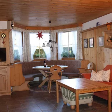 Ein gemütliches Wohnzimmer mit Holzverkleidung, einem roten Sofa und einem runden Esstisch. Große Fenster lassen viel Licht herein und schaffen eine einladende Atmosphäre.