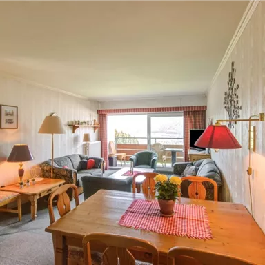 Ein komfortables Wohnzimmer mit gemütlichen Möbeln und viel natürlichem Licht. Der Raum enthält einen Esstisch, Pflanzen und eine Aussicht auf den Balkon.