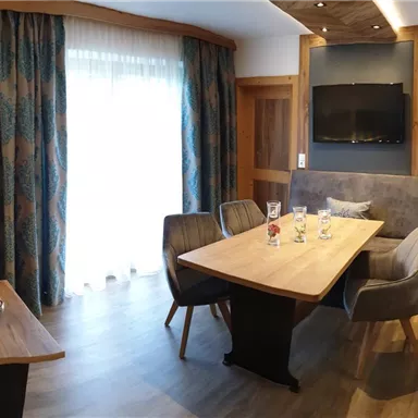 Ein modernes Wohnzimmer mit einer gemütlichen Couch und einem Esstisch. Große Fenster sorgen für viel natürliches Licht.