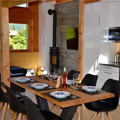 A modern kitchen with a wooden dining area. The room is bright and inviting, with large windows and cozy furnishings.