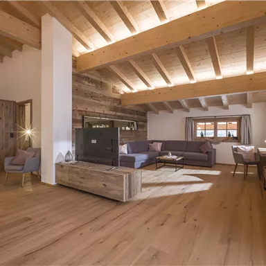 Ein modernes Wohnzimmer mit einer hohen Holzdecke und einem großen Fenster. Die Einrichtung ist gemütlich und aus natürlichen Materialien.