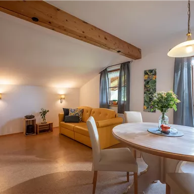 A cozy living space with a yellow sofa and a dining table. Large windows let in plenty of light and offer a view of nature.