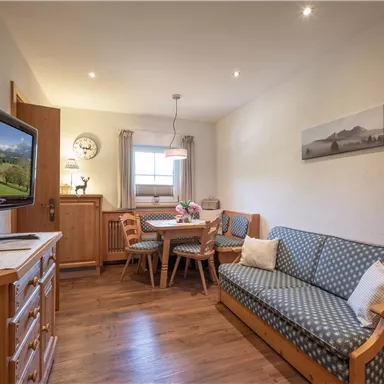 A cozy living space with a sofa, a table, and chairs. A television and a picture of the landscape are hanging on the wall.