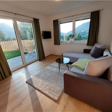A cozy living space with a sofa and a small table. Large windows offer a view of nature.