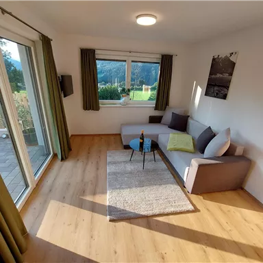 A bright living room with a cozy sofa and a table. Large windows offer a view of the outdoors and let in plenty of light.