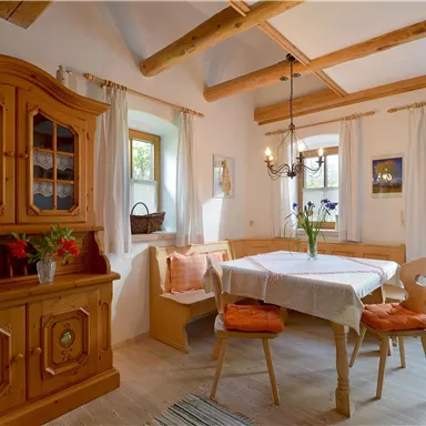 A cozy dining room with a wooden table and chairs. There is a wooden display case and plenty of daylight through the windows.
